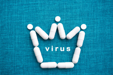 The crown sign is laid out of white capsules on a blue background. Inside is the word virus. The concept of the treatment of dangerous deadly coronavirus. Free space