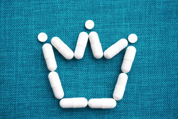 The crown sign is laid out of white capsules on a blue background.  The concept of the treatment of dangerous deadly coronavirus. Free space