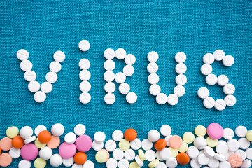 The inscription virus made of white capsules on a blue background. Below is a scattering of multi-colored tablets. The concept of the treatment of dangerous deadly coronavirus. Free space