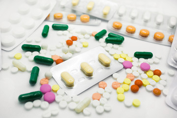The concept of pills for treatment. Multi-colored white,  yellow, orange, green, pink tablets on a white isolate background .  Blisters with capsules. Copy space. Place for text.