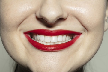Delighted smile. Close-up shoot of female mouth with bright red gloss lips make-up and well kept cheeks skin. Cosmetology, medicine, dentistry and beauty care, emotions and facial expression concept.