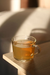 Cup of herbal tea on a living room table, illuminated by sunlight. Selective focus.