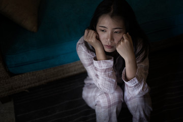 young beautiful sad and depressed Asian Japanese woman in pajamas at home sitting by living room couch feeling unhappy and confused suffering broken heart