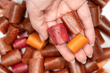 Closeup top view photography of female hand holding tasty healthy homemade organic dessert made of different kinds of fruits. Rolls of dried fruit leather perfect for eating as healthy snack.