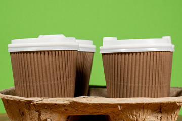 Closeup view photography of set of 4 brown paper coffee cups covered with white plastic lids standing in carton holder carry tray to take drinks away isolated on green background. 
