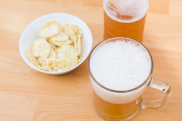 Beer mug full of beer and chips in a white plate on the white background 