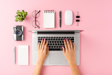 Woman’s hands using laptop on pink table with accessories. Business background. Top view