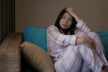 Fototapeta premium young beautiful sad and depressed Asian Japanese woman in pajamas at home sitting by living room couch feeling unhappy and confused suffering broken heart pain
