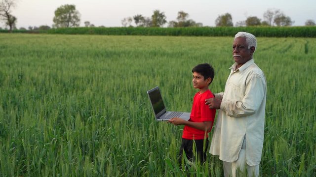 Young Indian Child Using Laptop With His Grandfather At Wheat Field