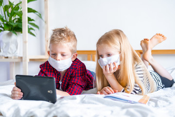 Distance learning online education. Sickness school boy and girl in medical mask studying at home with digital tablet laptop notebook and doing homework. Sitting on bed with training books.