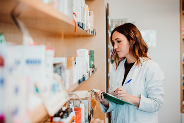 .Young female pharmacist working in her large pharmacy. Placing medications, taking inventory with...