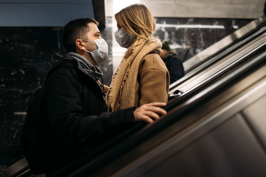 Young man and blonde woman looking at each other in medical masks on escalator in subway.