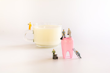 Health care and dental concept. Miniature teamwork on cup of milk and denture on white background.