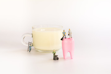 Health care and dental concept. Miniature teamwork on cup of milk and denture on white background.