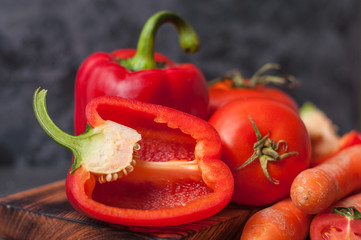 Vegetables carrots, tomatoes, sliced peppers close-up on a kitchen cutting board, on a dark concrete surface, side view