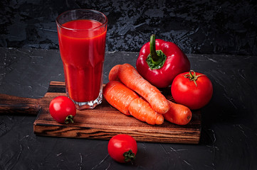 Vegetable juice in a glass and vegetables on a cutting board: carrots, peppers and tomatoes