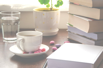 The white paper lies on a wooden table next to a stack of colorful books, a cup of coffee and a pot against
