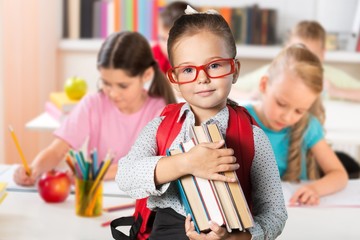 Cute little schoolgirl in glasses holding books
