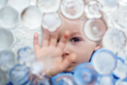 Portrait of blond toddler boy, lying under ice cubes, looking at camera
