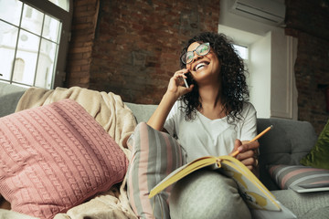 Talking on phone. Woman, freelancer during the work in home office while quarantine. Young female businesswoman staying at home, isolated. Using gadgets. Remote work, coronavirus spread prevention.