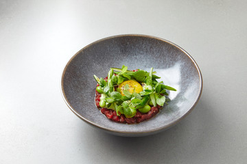 tartare with egg, green beans, herbs and spices in gray bowl