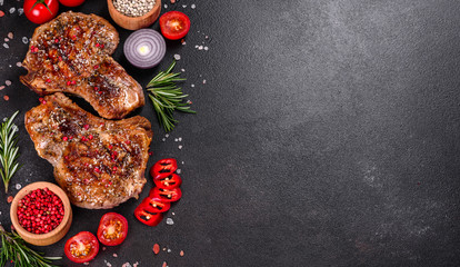 Fresh delicious juicy steak on the bones with vegetables and spices against a dark background