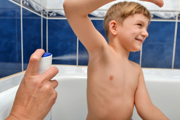 Mom sprays a deodorant boy after bathing in the shower room. © andov