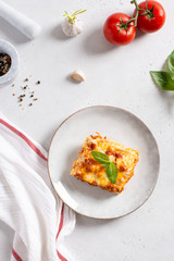 Tasty lasagna with meat and cheese on a plate, top view. Traditional italian lasagna with vegetables, basil, minced beef meat, tomato and cheese on white concrete background. Restaurant menu, recipe