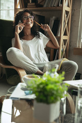 Talking on phone. Woman, freelancer during the work in home office while quarantine. Young female businesswoman staying at home, isolated. Using gadgets. Remote work, coronavirus spread prevention.