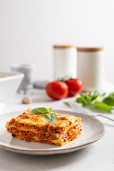Tomato and ground beef lasagne with cheese and tomatoes layered between sheets of traditional Italian pasta served on a gray plate. Italian menu recipe. Side view, copy space. Tasty homemade lasagna