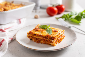 Piece of tasty hot lasagna served with a basil leaf on a gray plate. Italian cuisine, menu, recipe. Homemade meat lasagna. Close up - obrazy, fototapety, plakaty