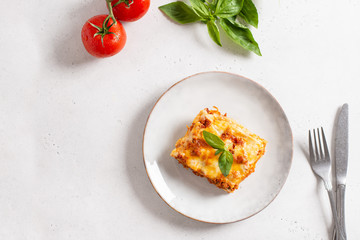 Piece of tasty hot lasagna served with a basil leaf on a gray plate. Italian cuisine, menu, recipe. Homemade meat lasagna. Copy space, top view - obrazy, fototapety, plakaty