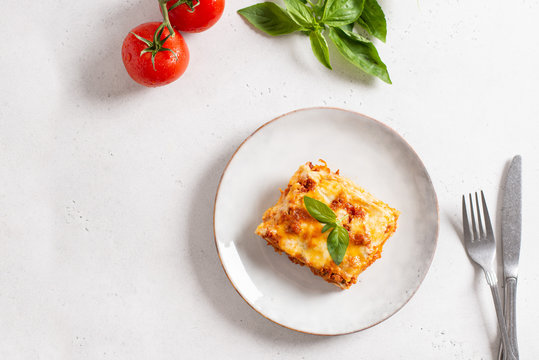 Piece of tasty hot lasagna served with a basil leaf on a gray plate. Italian cuisine, menu, recipe. Homemade meat lasagna. Copy space, top view