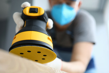 Male handy man hold yellow grinder with disc sander in hand closeup background. Professional...