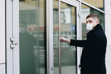 Young man opening door to his office wearing surgical face mask to protect from coronavirus covid-19 virus global pandemic
