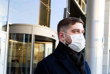 Fototapeta na wymiar Handsome Caucasian young man near his office wearing surgical face mask during global coronavirus covid-19 virus epidemic