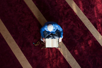 Young Arabic Muslim man reading Koran and praying. Religious muslim man reading holy koran inside the mosque.
