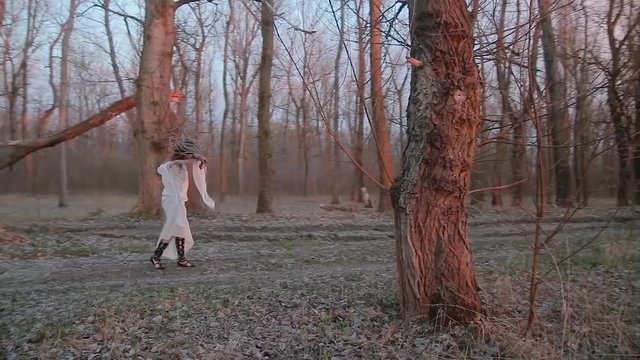Cute young woman in image of witch and old Slavic costume runs through forest and performs movements corresponding to her image