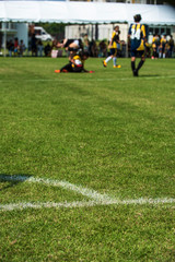 Soccer pitch for a girl youth tournament, seeing a goal keeper sitting on a pitch with ball safety in her hands during a game.