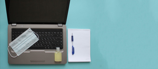 Notepad, pen, antiseptic, medical mask and laptop on a blue background. The concept of remote work...