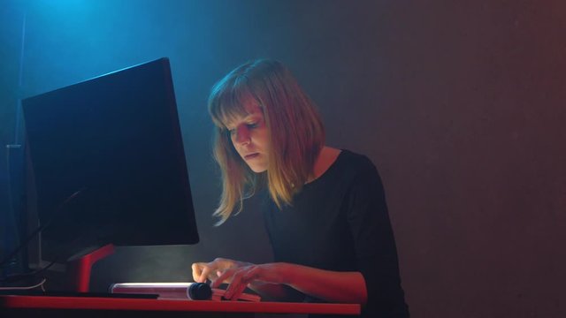 Hacker girl organizes malware attack on global scale. She working on a computer while the smoke spreads around in the underground office space. Neon light flickers in a dark room. Digital resistance