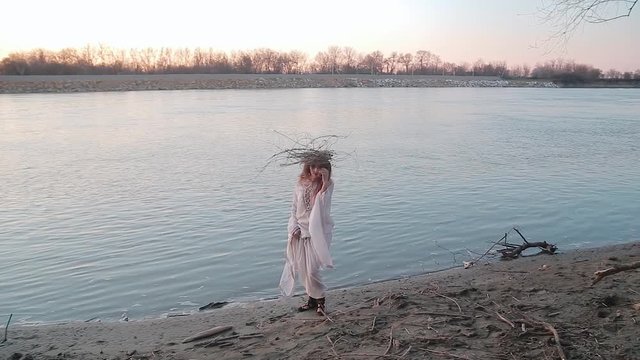 Pretty young woman in the image of witch and old Slavic costume runs on Bank of river near forest