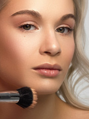 Beauty close-up of a blond woman applying powder to clean her face skin. Looks at the camera with a...