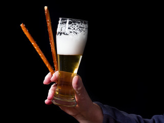 main qui tient un verre de bi&egrave;re et des bretzels sur fond noir