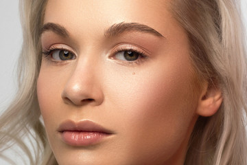 Fototapeta premium Beauty close-up of a blond woman applying powder to clean her face skin. Looks at the camera with a sexy look. Soft skin care, natural makeup. Pink lip gloss, smooth and thick eyebrows. curly hair