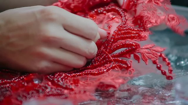 Close up female hands embroidery pattern on red fabric with beads and needle and thread