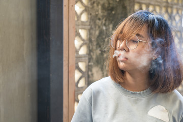 Portrait of fashion woman smoking while wearing glasses against brick wall