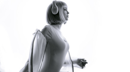 Obraz premium Beautiful woman in futuristic costume over white background. Black and white portrait of young girl in modern headphones listening music. Free space for text.