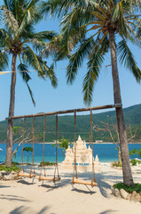 Swing on the beach between palm trees and sand sculpture in the tropics