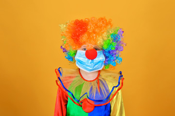 Sad and sad baby clown in a protective medical mask from coronavirus on a yellow background.